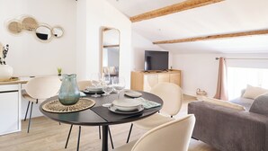 A modern living room with a dining area, featuring a round table set for four, a sofa, and a television. -  Le Gratien by Béziers 1609 Résidences (Béziers)