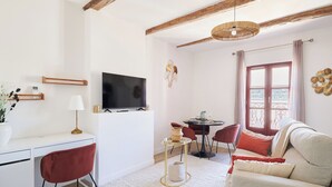 A modern living room with a flat-screen TV, a dining area with a table and chairs, and a large window with curtains. -  Le Gratien by Béziers 1609 Résidences (Béziers)
