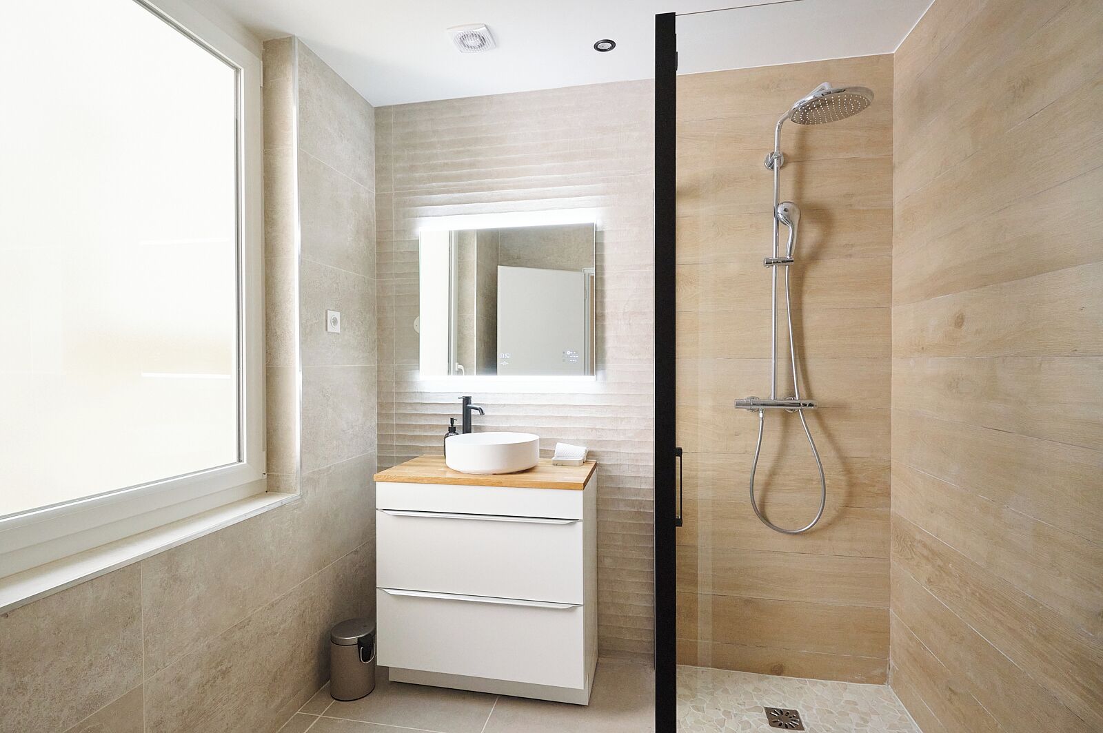 Un baño moderno con un ventanal grande, un lavabo redondo, un espejo y una ducha.