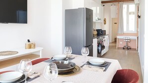 Un comedor con una mesa dispuesta para cuatro, una cocina moderna al fondo y vigas de madera a la vista en el techo.