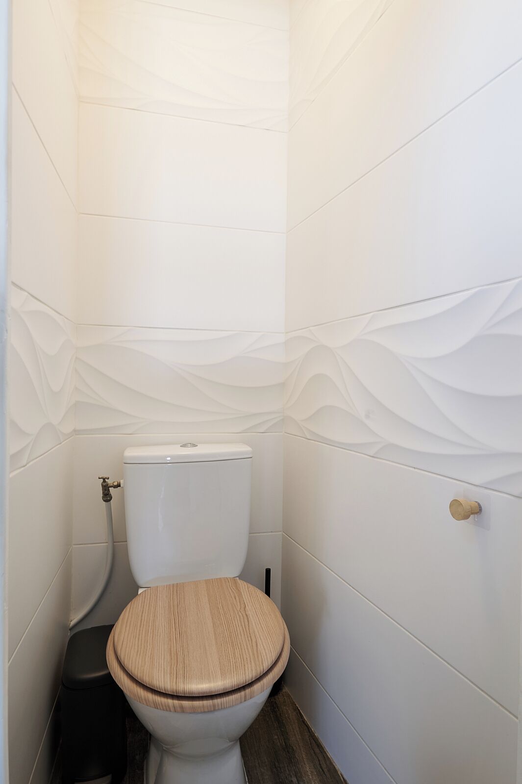 Une petite salle de bain moderne avec des toilettes blanches, un abattant en bois et une poubelle noire.