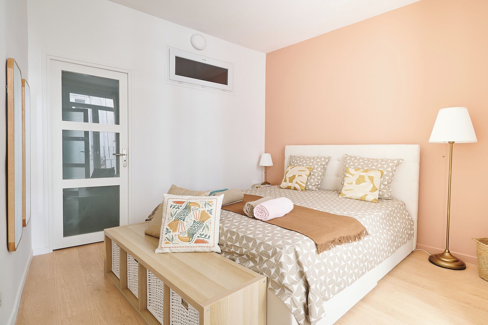 Un dormitorio con cama, mesitas de noche, un banco, una lámpara y una ventana.