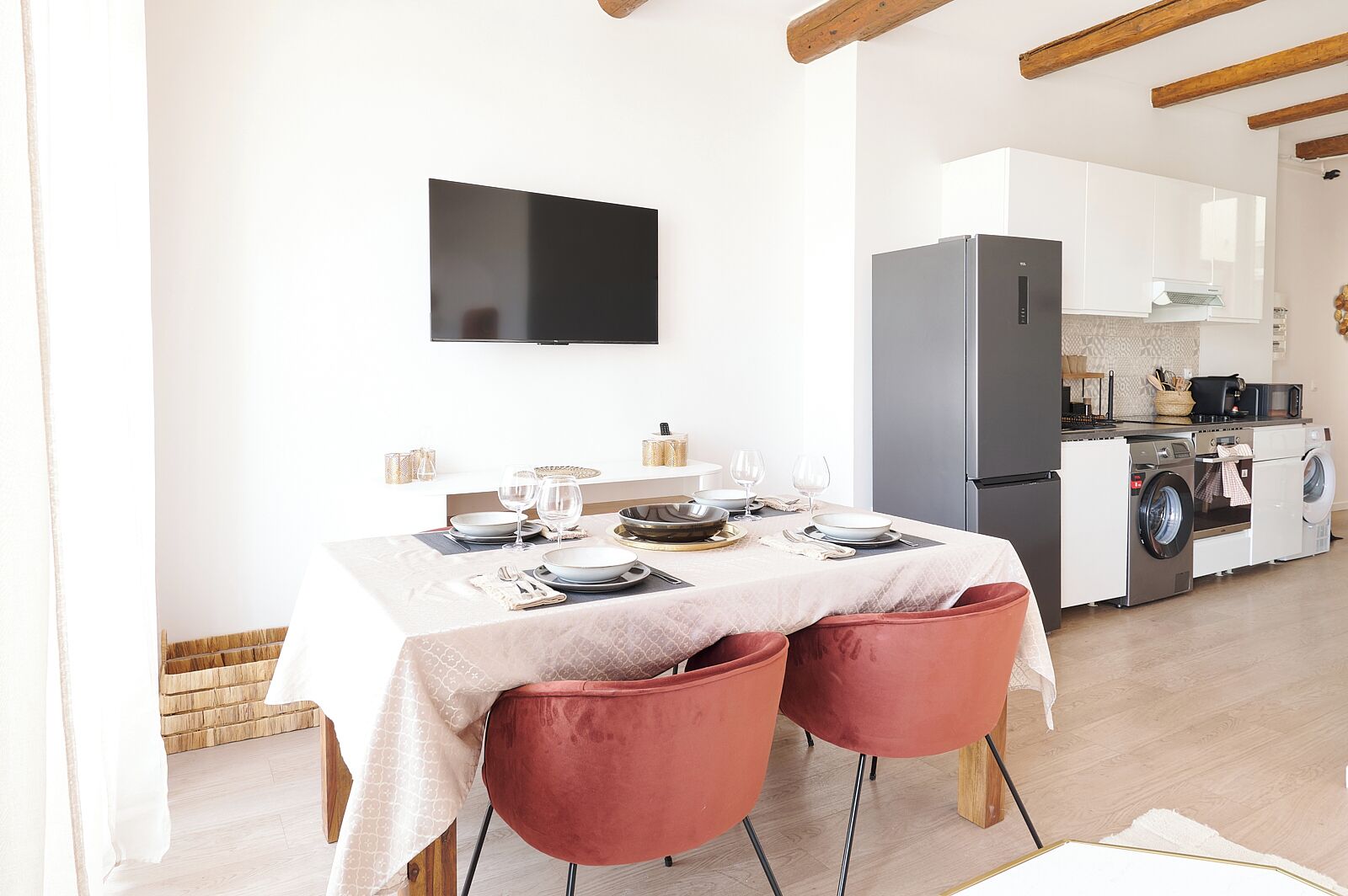 A modern kitchen with a dining area, a flat-screen TV, a washing machine, and a refrigerator.