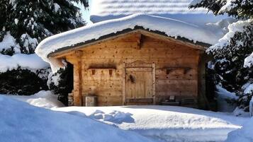 A wooden cabin with a snow-covered roof, surrounded by snow and trees.
