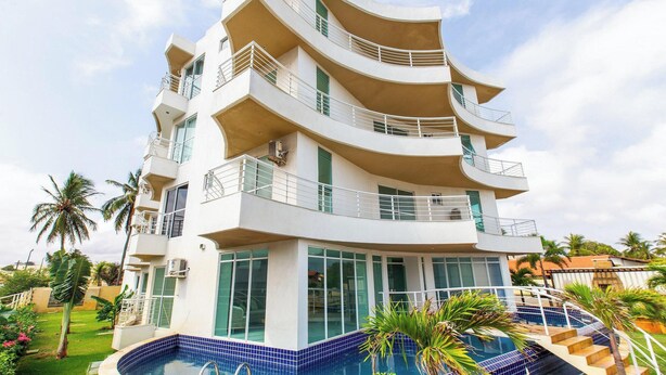 Un hotel de varios pisos con balcones, piscina y exuberante paisaje tropical.
