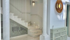 Een statige trap met marmeren treden en witte leuningen, omlijst door witte kolommen en een decoratief wandpaneel.
