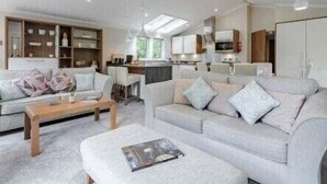 A modern living room with a sofa, a coffee table, and a kitchen area in the background. - Guelder Rose Lodge - Kelling Heath Holiday Park - 22249 (Holt)