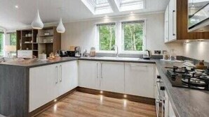 A modern kitchen with skylights, white cabinets, and a central island. - Guelder Rose Lodge - Kelling Heath Holiday Park - 22249 (Holt)