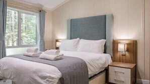 A bedroom with a bed, bedside tables, and a window. - Guelder Rose Lodge - Kelling Heath Holiday Park - 22249 (Holt)