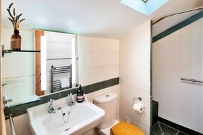A bathroom with a glass shelf, a sink, a toilet, and a shower. - Little Roost (Lyme Regis)