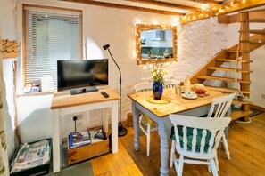 A cozy dining area with a wooden table, white chairs, a vase with flowers, and a mirror with lights. - Little Roost (Lyme Regis)