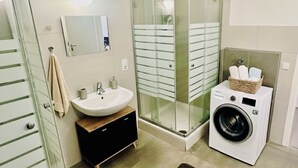 A modern bathroom with a glass shower enclosure, a sink, a washing machine, and a mirror. - City Residenz Karlsruhe – upscale living in the heart of the city (Karlsruhe)
