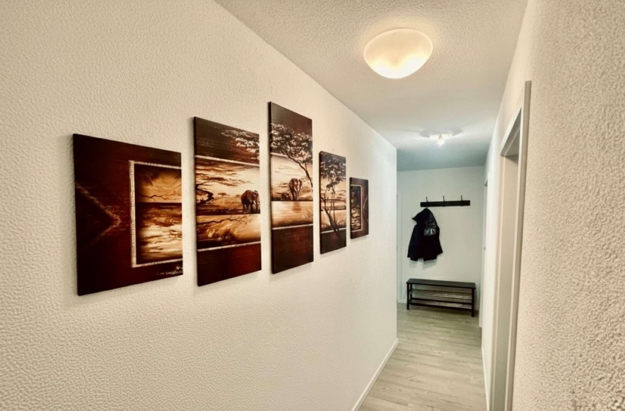 Un couloir orné d’une série de tableaux encadrés, un porte-manteau avec une veste, et un banc.