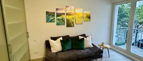 Una sala de estar moderna con un sofá marrón oscuro, una mesita redonda y un conjunto de cuatro cuadros de paisajes en la pared.