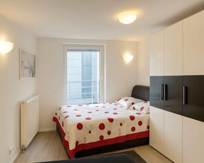 Quarto com cama, radiador, janela com persianas e guarda-roupa.