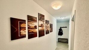 A hallway with four framed pictures on the wall, a coat rack with a jacket, and a bench. - City Residenz Karlsruhe – upscale living in the heart of the city (Karlsruhe)