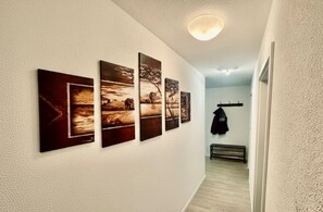 A hallway with four framed pictures on the wall, a coat rack with a jacket, and a bench. - City Residenz Karlsruhe – upscale living in the heart of the city (Karlsruhe)