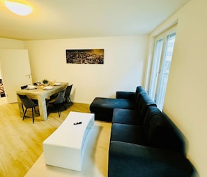 A living room with a sofa, a dining table with chairs, and a small white table. - City Residenz Karlsruhe – upscale living in the heart of the city (Karlsruhe)