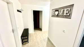 A hallway with a 'HOME' sign on the wall, a door on the left, and a dark-colored bench in the center. - City Residenz Karlsruhe – upscale living in the heart of the city (Karlsruhe)