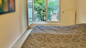 A bedroom with a patterned bedspread, a ceiling light, a window with blinds, and a painting on the wall. - City Residenz Karlsruhe – upscale living in the heart of the city (Karlsruhe)