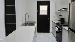 A modern kitchen with a black door, white cabinetry, a stainless steel sink, and a built-in oven.