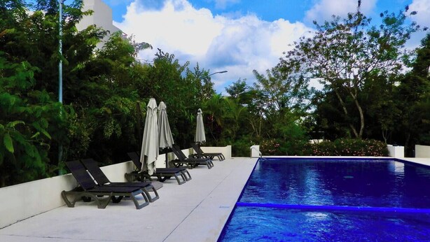 A swimming pool with lounge chairs and umbrellas, surrounded by greenery.