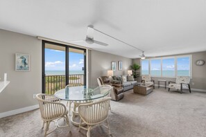 A spacious living area with a glass table, white wicker chairs, a leather sofa, and a view of the ocean through large windows. - Welcome to Loggerhead Cay 503, a beachfront corner condo with two private lanais showcasing breathtaking sunrise and sunset views. Sleeps 6 with beach gear, heated pool, tennis, pickleball, in-unit washer/dryer, and direct beach access. (Sanibel Island)