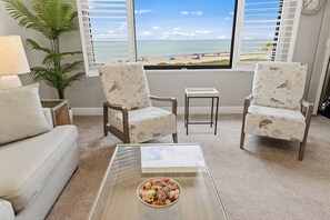 A living room with a view of the beach, two patterned chairs, a small table, and a lamp. - Welcome to Loggerhead Cay 503, a beachfront corner condo with two private lanais showcasing breathtaking sunrise and sunset views. Sleeps 6 with beach gear, heated pool, tennis, pickleball, in-unit washer/dryer, and direct beach access. (Sanibel Island)