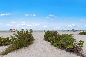 Ein Strand mit einem sandigen Pfad zum Meer, Sonnenschirmen und Liegestühlen.