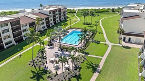 Ein Resort mit einem zentralen Pool, umgeben von Palmen und Außenbereich-Sitzgelegenheiten, mit Blick auf einen Strand und den Ozean.
