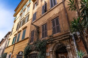 A multi-story building with a yellow facade, green shutters, and an arched entrance. - Quiet Elegance Retreat Apartment Trastevere Family-friendly (Roma)