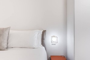 A neatly made bed with white and grey bedding, a small orange nightstand, and a wall-mounted light fixture. - Quiet Elegance Retreat Apartment Trastevere Family-friendly (Roma)