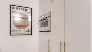 A kitchen with a framed poster of a spaghetti advertisement, a modern oven, and gold handles on the cabinets. - Quiet Elegance Retreat Apartment Trastevere Family-friendly (Roma)