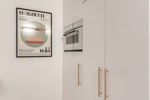 Eine Küche mit einem gerahmten Poster einer Spaghetti-Werbung, einem modernen Backofen und goldenen Griffen an den Schränken.