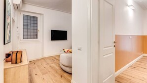A room with a wooden floor, a white door, a television mounted on the wall, and a window with a grid pattern. - Quiet Elegance Retreat Apartment Trastevere Family-friendly (Roma)