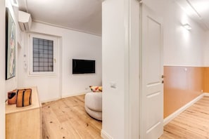 Ein Zimmer mit Holzboden, einer weißen Tür, einem an der Wand befestigten Fernseher und einem Fenster mit Gittermuster.