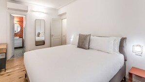 A modern bedroom with a large bed, a bedside table, a mirror, and a door leading to a bathroom. - Quiet Elegance Retreat Apartment Trastevere Family-friendly (Roma)