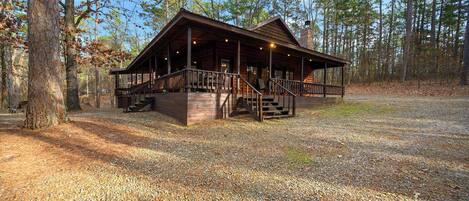 A cabin with a porch and stairs, surrounded by trees.