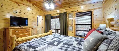 Une chambre dans un chalet en bois, avec un lit, une télévision, un ventilateur de plafond et une fenêtre avec des rideaux.