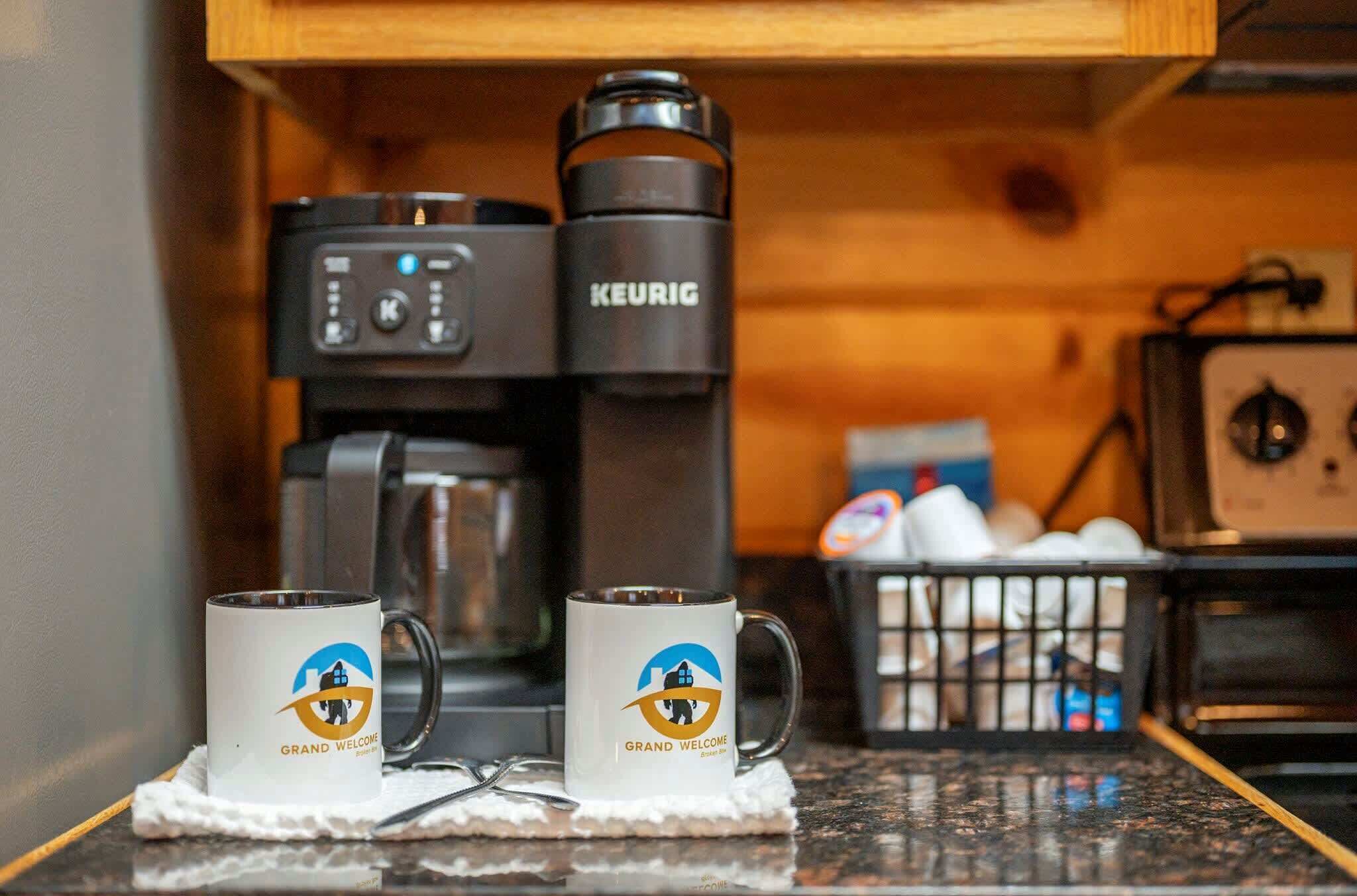 Una màquina de cafè, dues tasses amb un logotip i una cistella d'ous sobre una cuina.