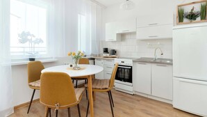 A modern kitchen with white cabinets, a dining table with chairs, a coffee maker, and a hanging plant. - Sunny Studio with Sea View | Balcony (Gdynia)