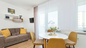 A modern living room with a sofa, two chairs, a round table, and a TV mounted on the wall. - Sunny Studio with Sea View | Balcony (Gdynia)