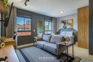 A modern hotel room with a sofa, a small table, a bed, and large windows offering a view of the outside. - Stay in Comfort and Convenience Near Ufsc - Ters (Florianópolis)