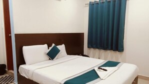 Een net opgemaakt bed met witte lakens en een turquoise accentkleur, een raam met turquoise gordijnen, en een luchtverwarmer aan de muur.