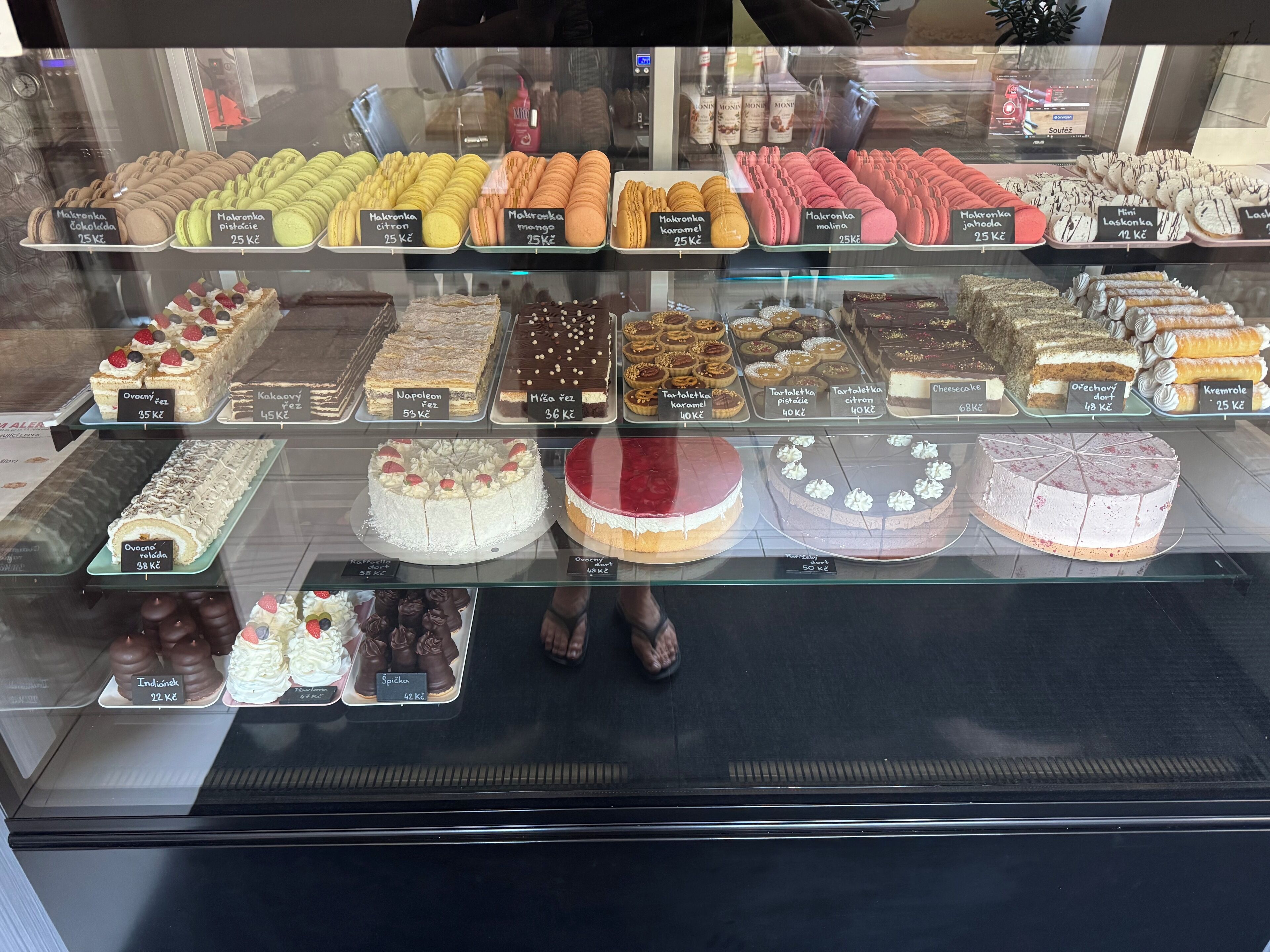 Leipomon vitriini, jossa on esillä erilaisia leivonnaisia ja kakkuja, kuten macaron-leivoksia, piirakoita sekä valikoima kakkuja erilaisilla kuorrutteilla ja mauilla.