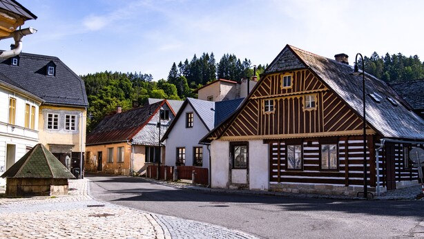 Eine Kopfsteinpflasterstraße gesäumt von traditionellen Gebäuden, darunter ein Holthaus mit geneigtem Dach und ein Steinhaus mit Giebeldach.