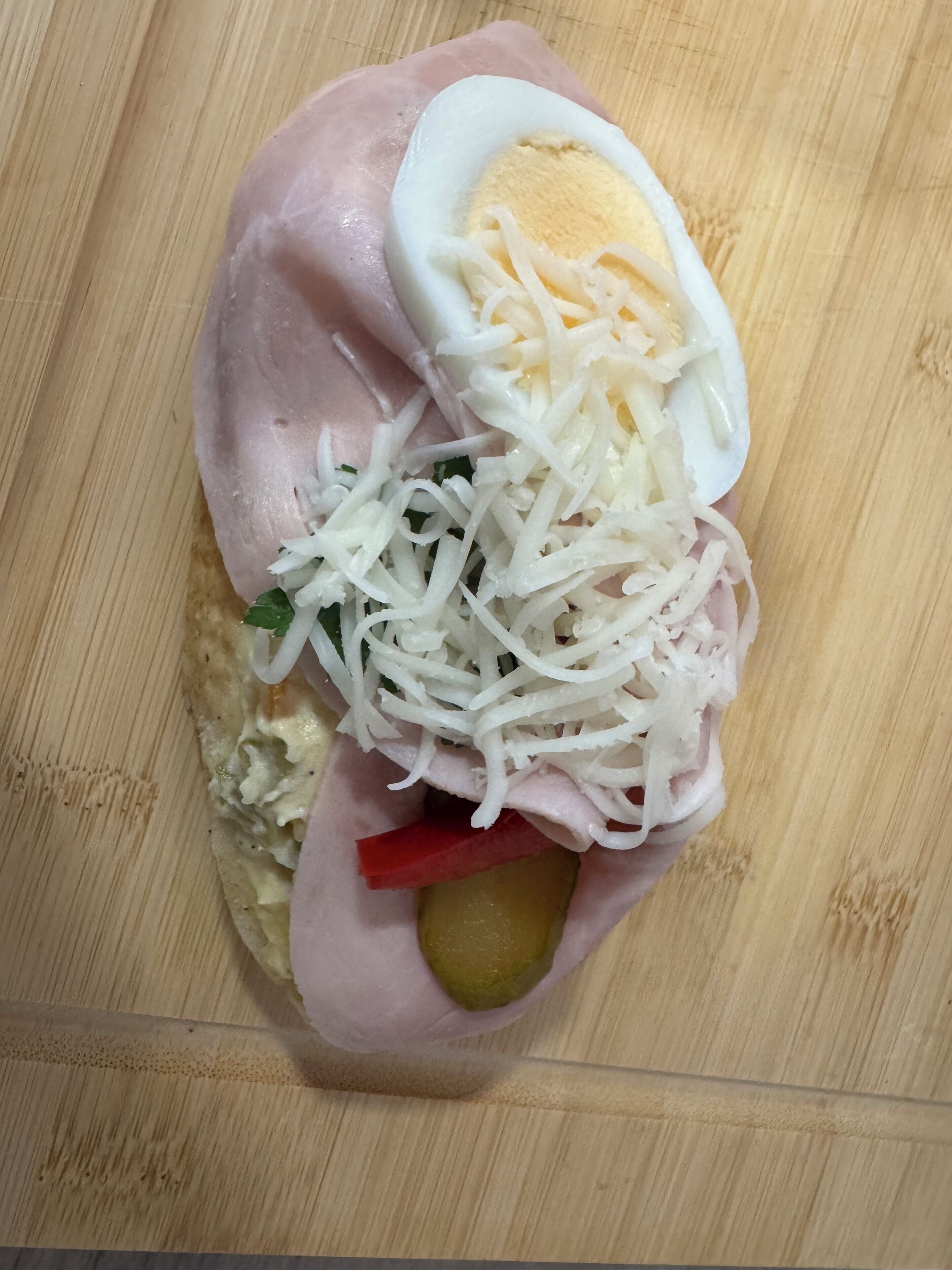 Ein Sandwich mit Schinken, Käse, Ei und einer Gewürzgurke auf einer Holzschneidebrett.