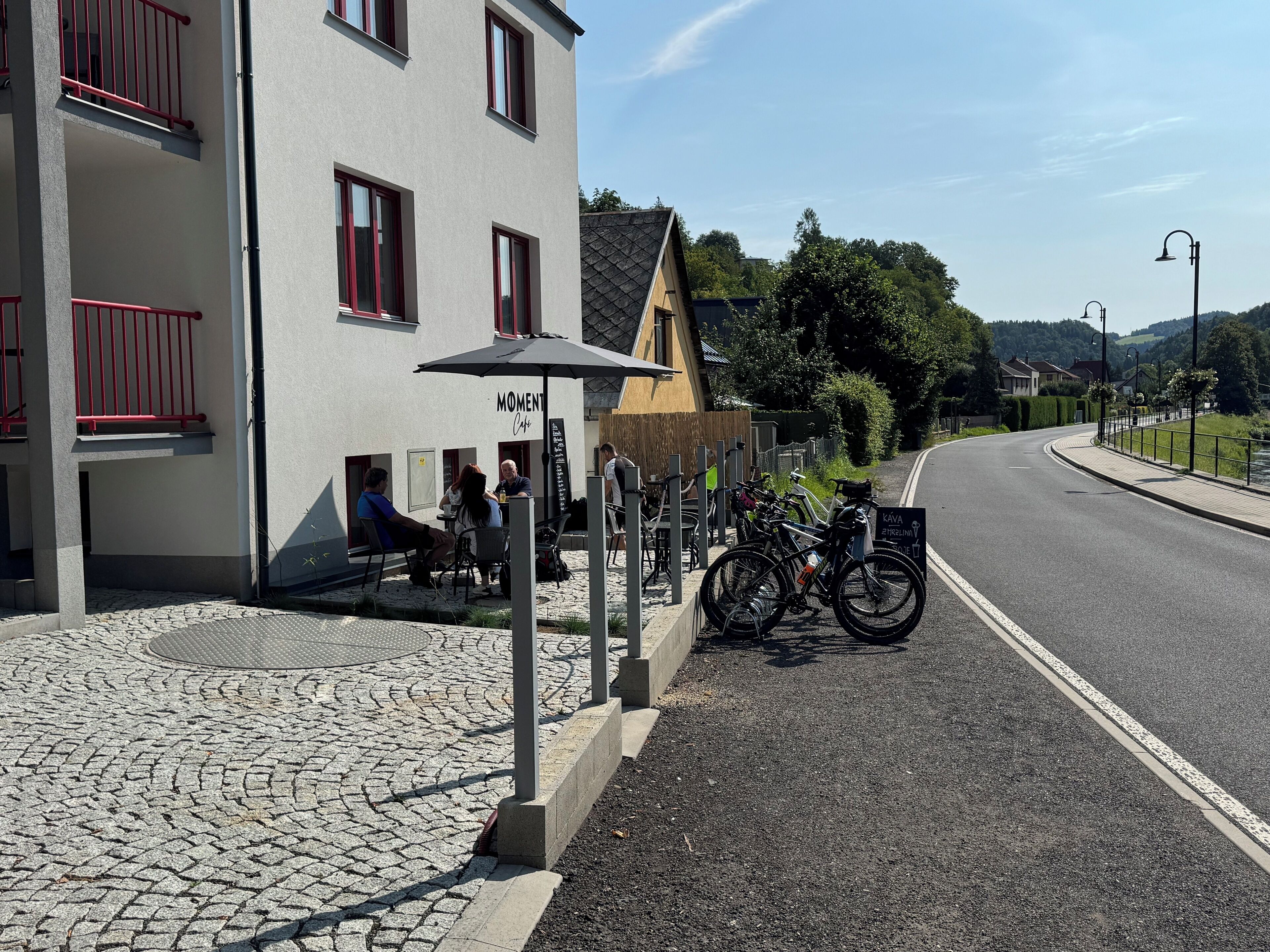 Un café appelé « Moment Café », doté d’une terrasse, avec des vélos garés à l’extérieur et un trottoir pavé.