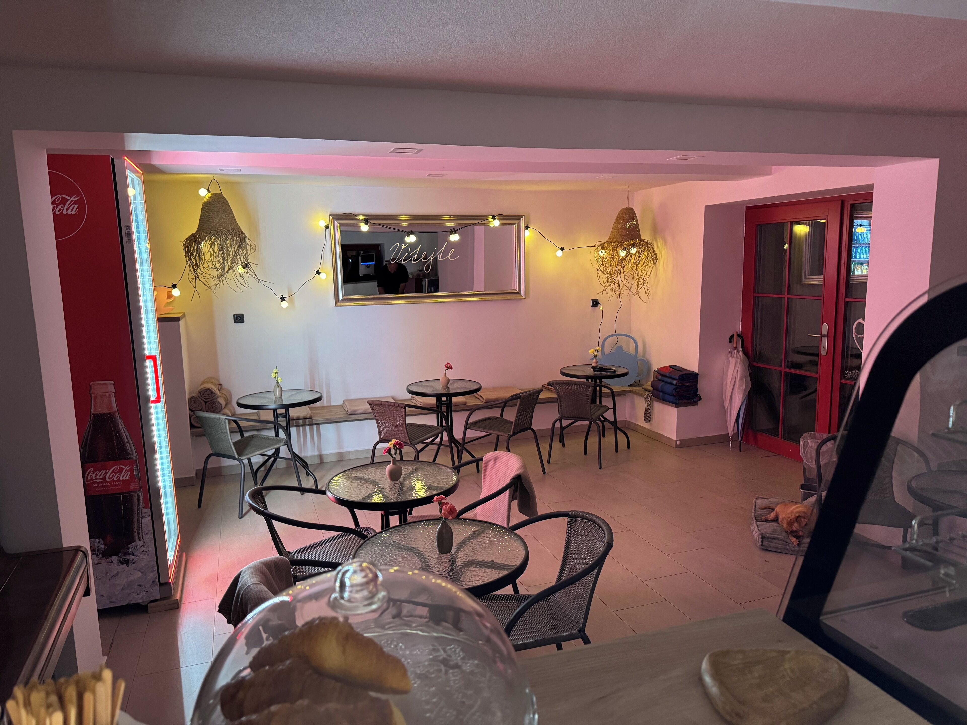 A cozy café with round tables and chairs, a mirror on the wall, and string lights.
