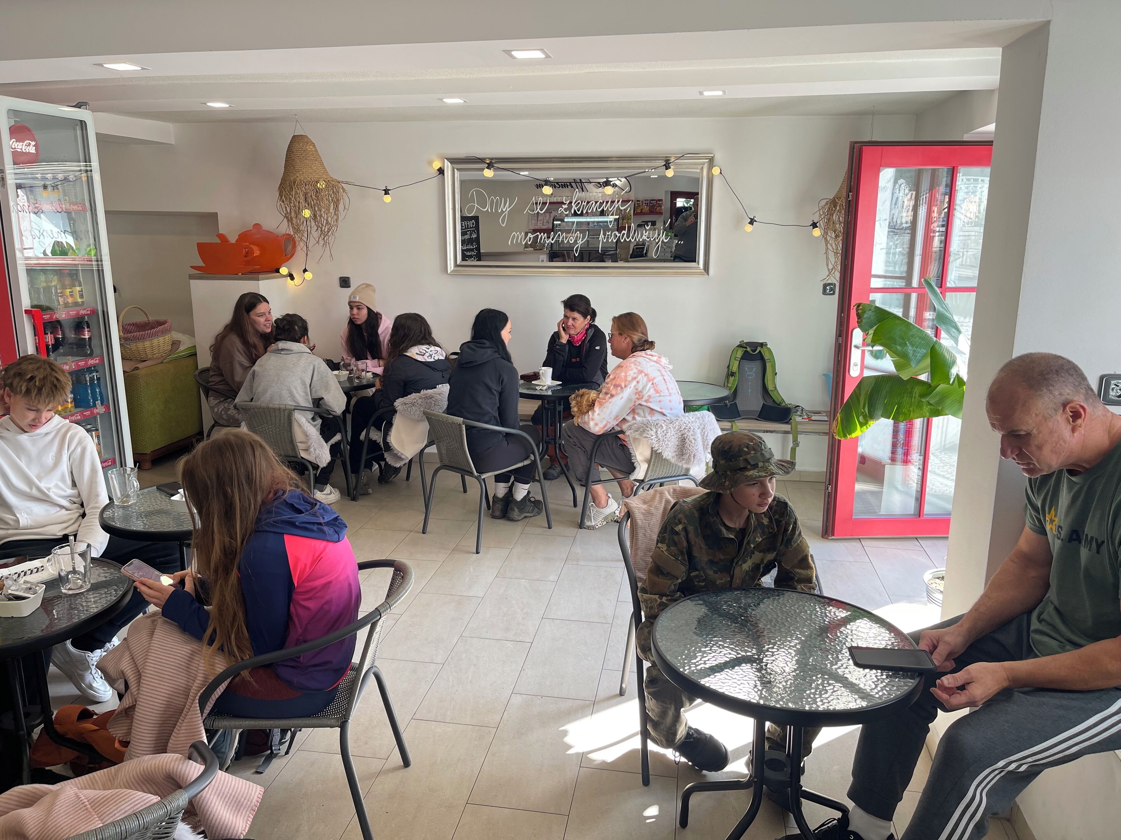 Un espace de restauration informel avec des tables et des chaises rondes, un réfrigérateur rempli de boissons et un miroir agrémenté de lumières décoratives.